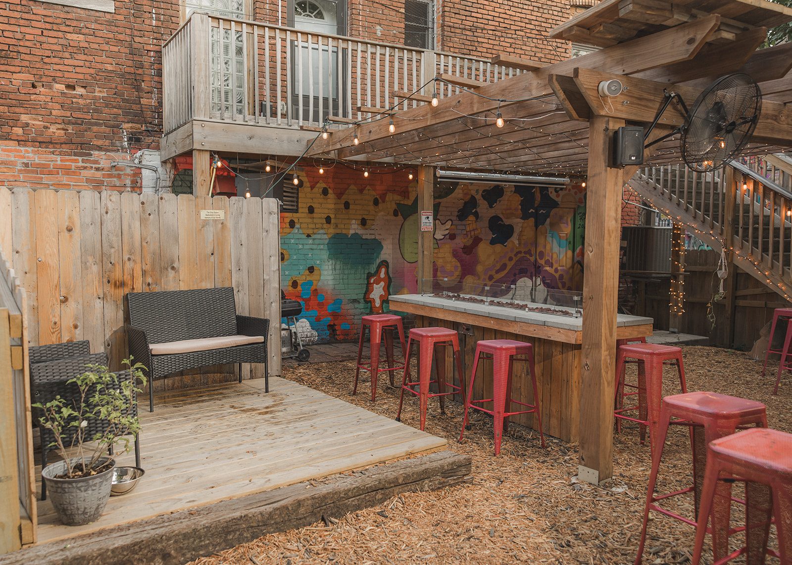 Covered outdoor bar with red stools and a raised deck with lounge chairs on the Border Brewing patio