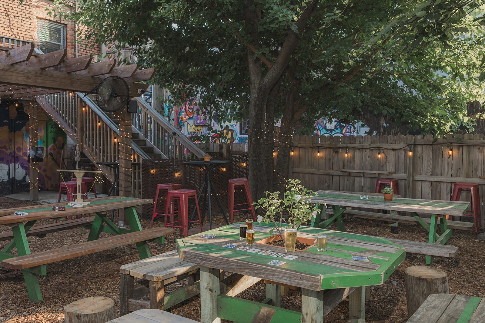 Green picnic tables and red stools under string lights on the patio in the evening