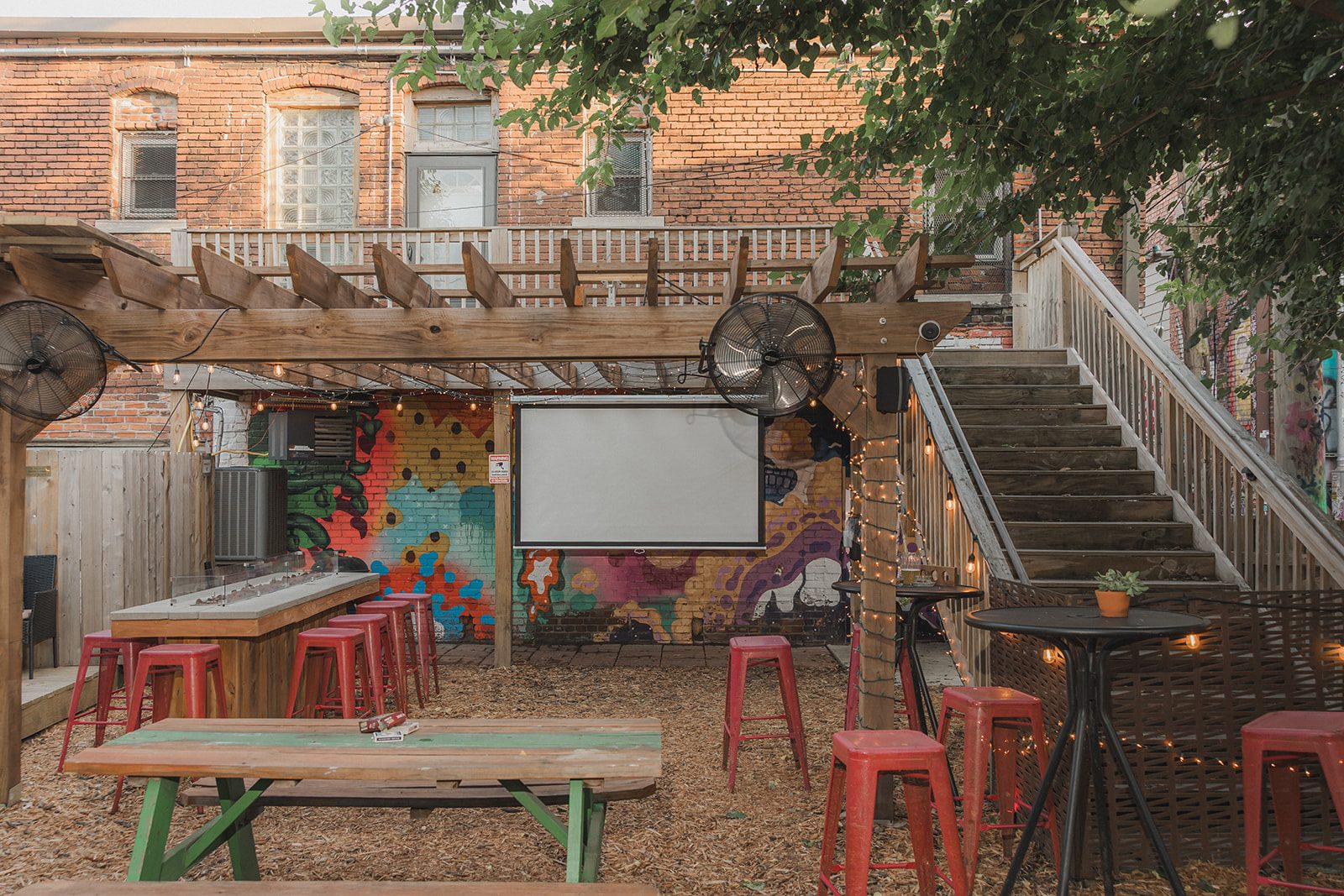 Projector screen mounted on the mural wall beside the outdoor bar rail and stools on the Border Brewing patio