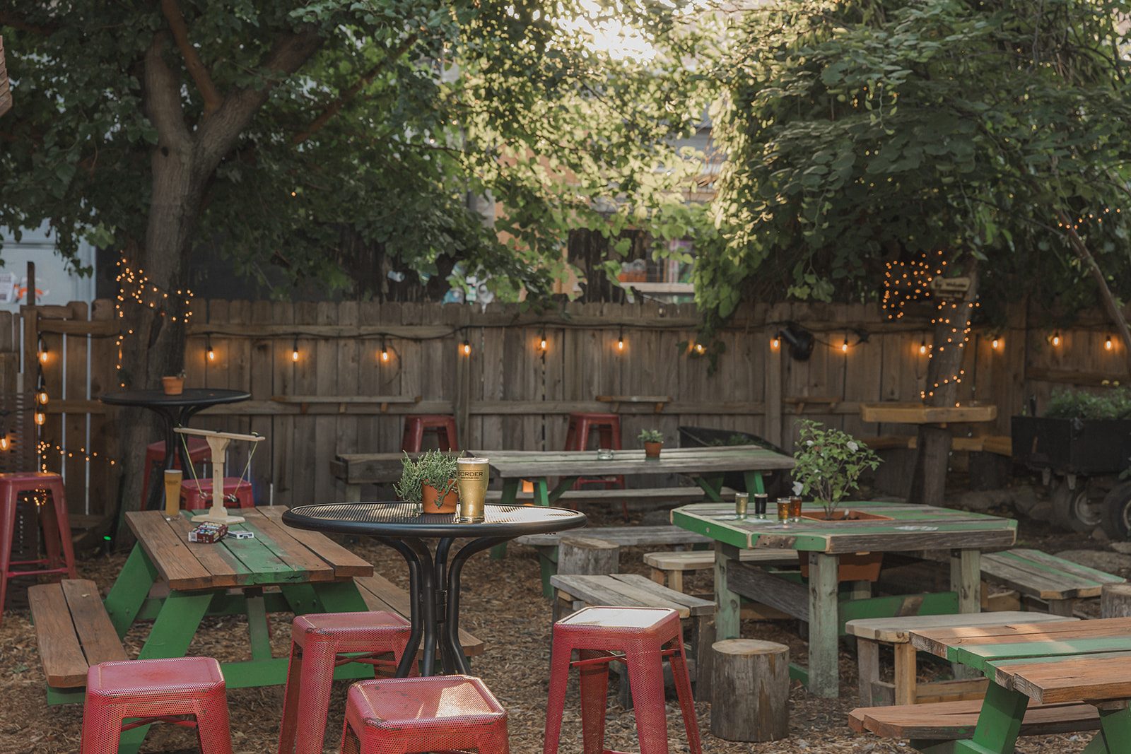 String lights glowing over picnic tables and red stools in The Backyard beer garden at Border Brewing Company in Kansas City's Crossroads Arts District