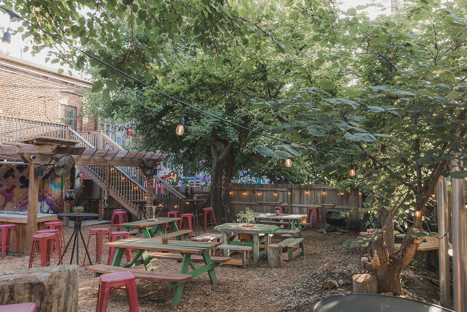 Mature shade trees over green and wood picnic tables in the beer garden patio at Border Brewing Company in Kansas City