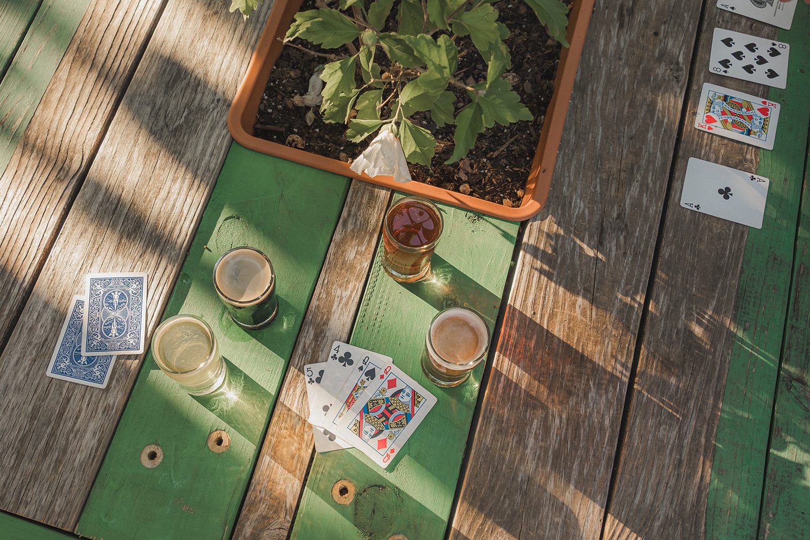 Overhead view of playing cards and craft beers spread across a green picnic table on the Border Brewing patio