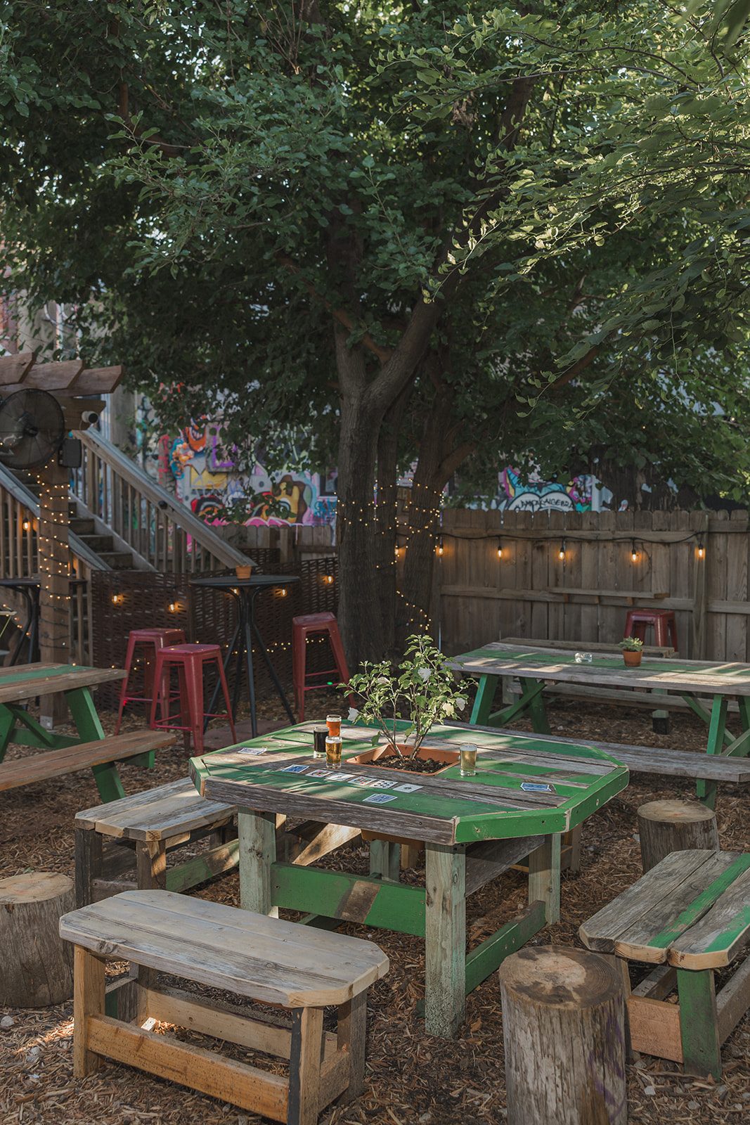 A green picnic table with a planter box and beers, lit by string lights on the Border Brewing patio