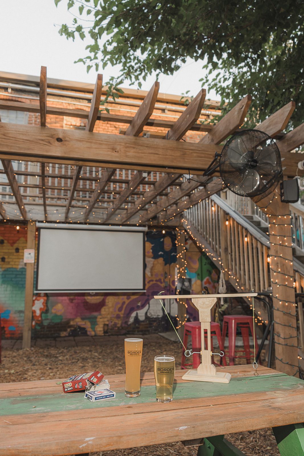 The projector screen and pergola fans seen from a patio table with beers in the foreground