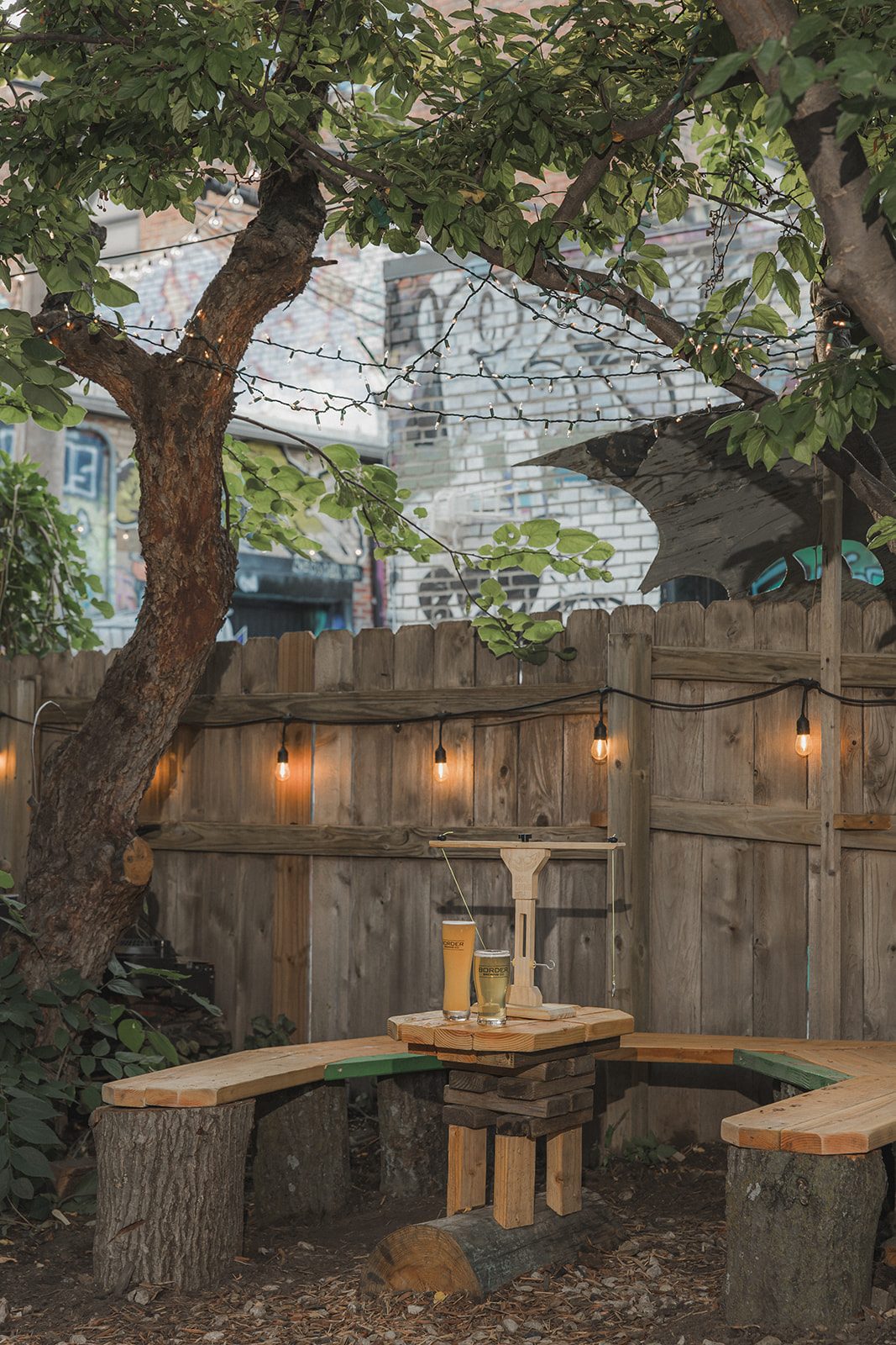 A pint glass resting on the wraparound tree bench under warm string lights on the Border Brewing patio