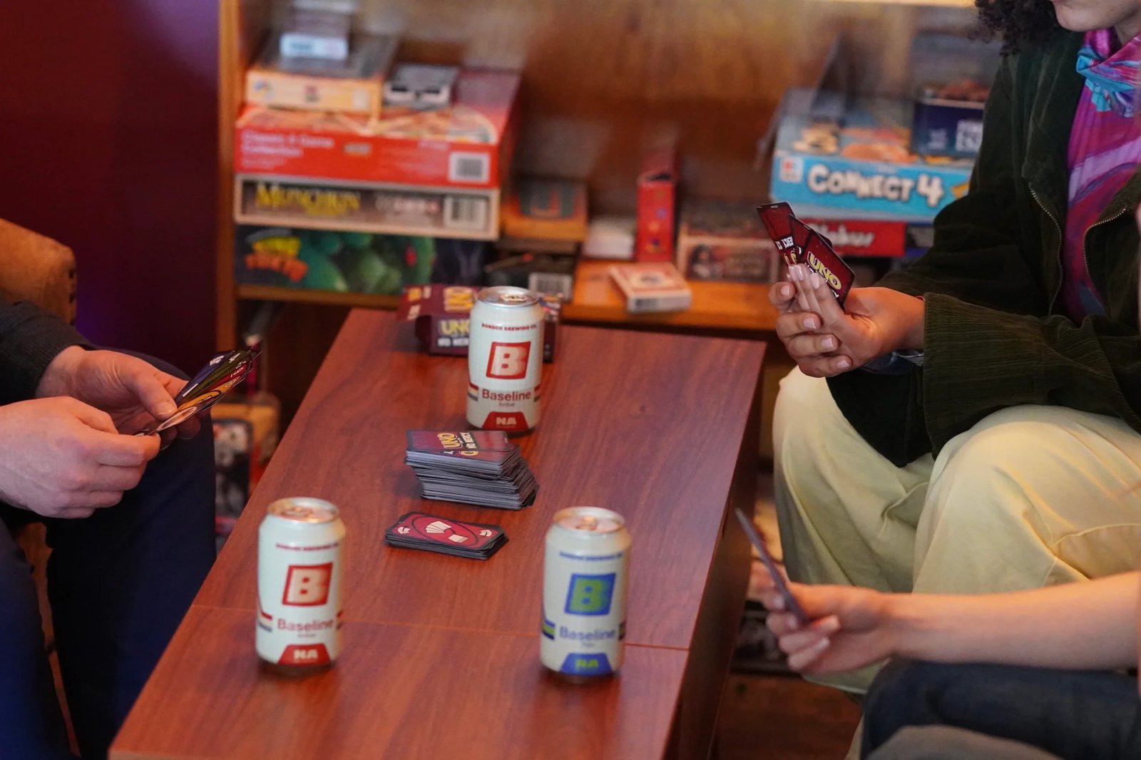 Two friends playing UNO at Border Brewing Company with Baseline Amber and Pale Ale NA cans on the table
