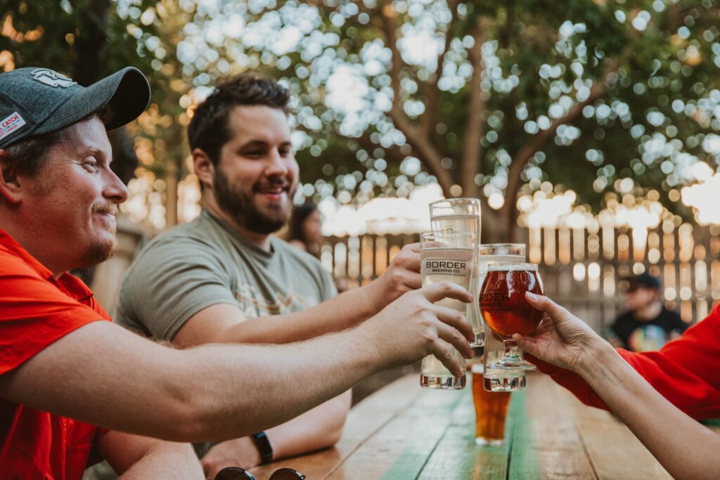 Group of friends clinking glasses and saying cheers on the Border Brewing Company patio in KC