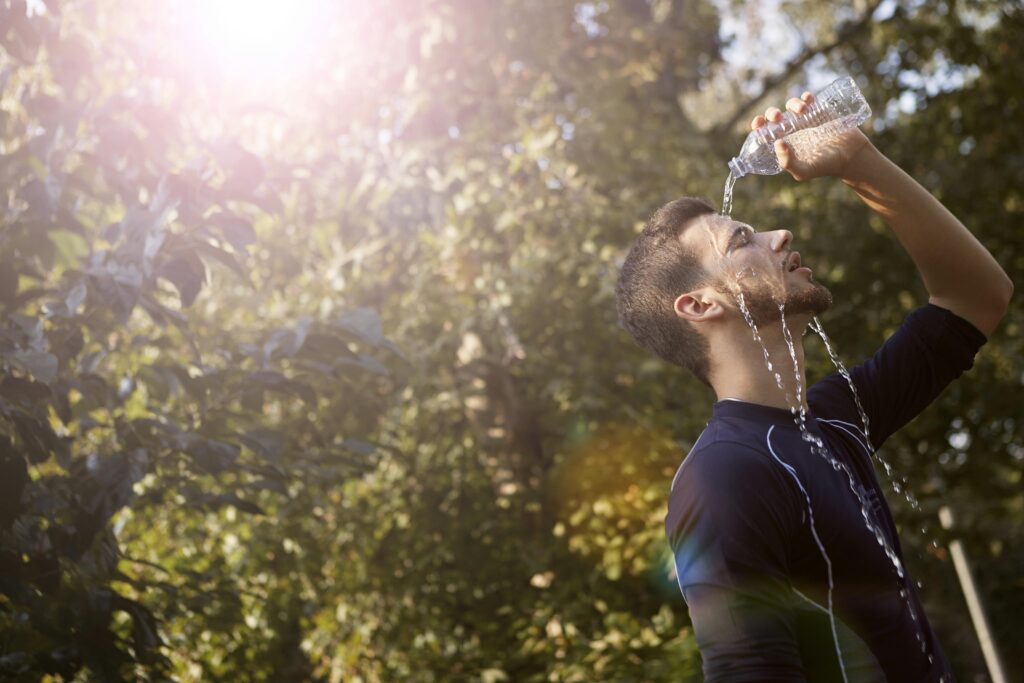 Young white male pouring a water bottle over him as he looks to hydrate himself.